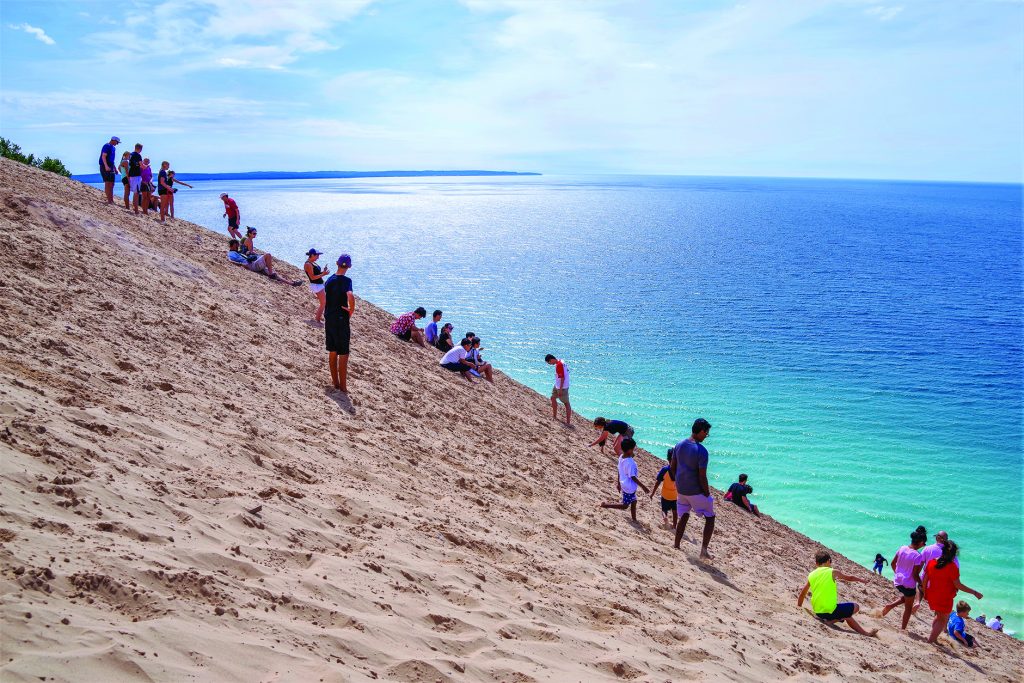 What A Grand View Across Lake Michigan. Public grouping on a steep sand dune overlook on shore of Lake Michigan at Sleeping Bear Dunes National Park on a sunny summer day with a blue sky and a vast view in Michigan, USA in August. (ID 190447459 © Schneidersimages | Dreamstime.com)